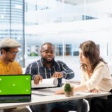 Clients negotiating with the realtor next to isolated copy space on laptop, examining layout and blueprints for a new high class office space. Business people investing in property with financier.