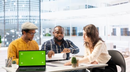 Clients negotiating with the realtor next to isolated copy space on laptop, examining layout and blueprints for a new high class office space. Business people investing in property with financier.