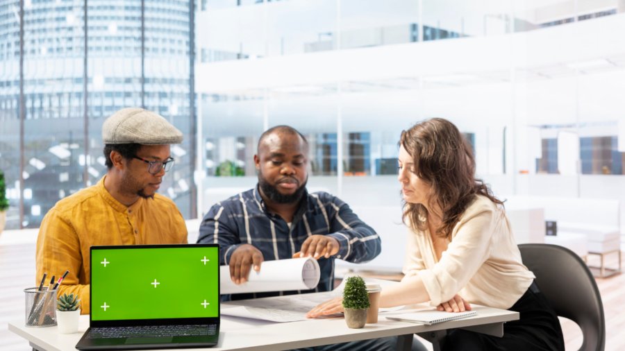 Clients negotiating with the realtor next to isolated copy space on laptop, examining layout and blueprints for a new high class office space. Business people investing in property with financier.